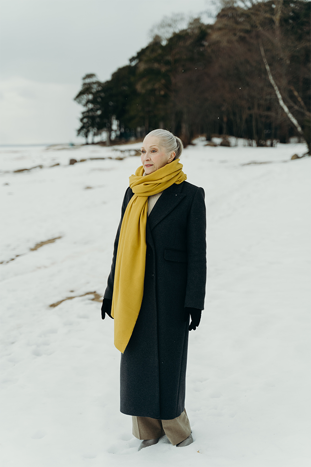 A woman on the beach in a scarf and long coat, showing the result if you reboot your style for ageless self-expression.