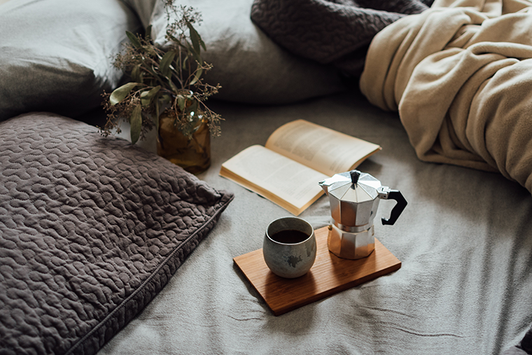 Coffee and a book on the bed, symbolizing how important it is to improve your day with a morning routine.